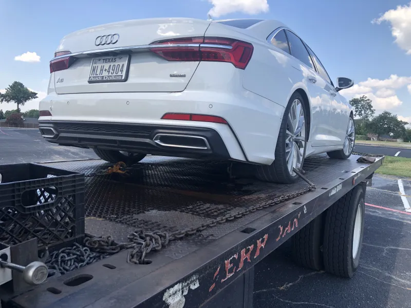Long distance towing driver on the phone next to a flatbed tow truck leaving Dallas, TX